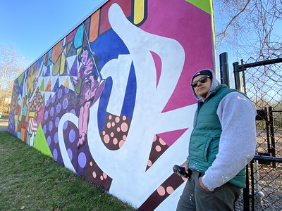 Photo of Artist Juan Pineda in front of on of his murals at Dewey Local Park