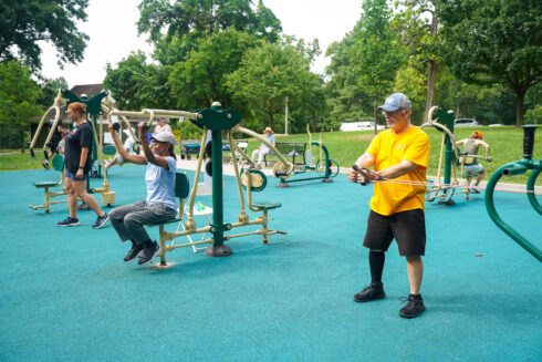 People using various workout machines at an outdoor exercise station.