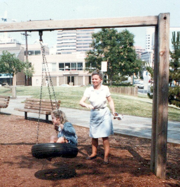 A woman pushes a young girl on a tire swing.