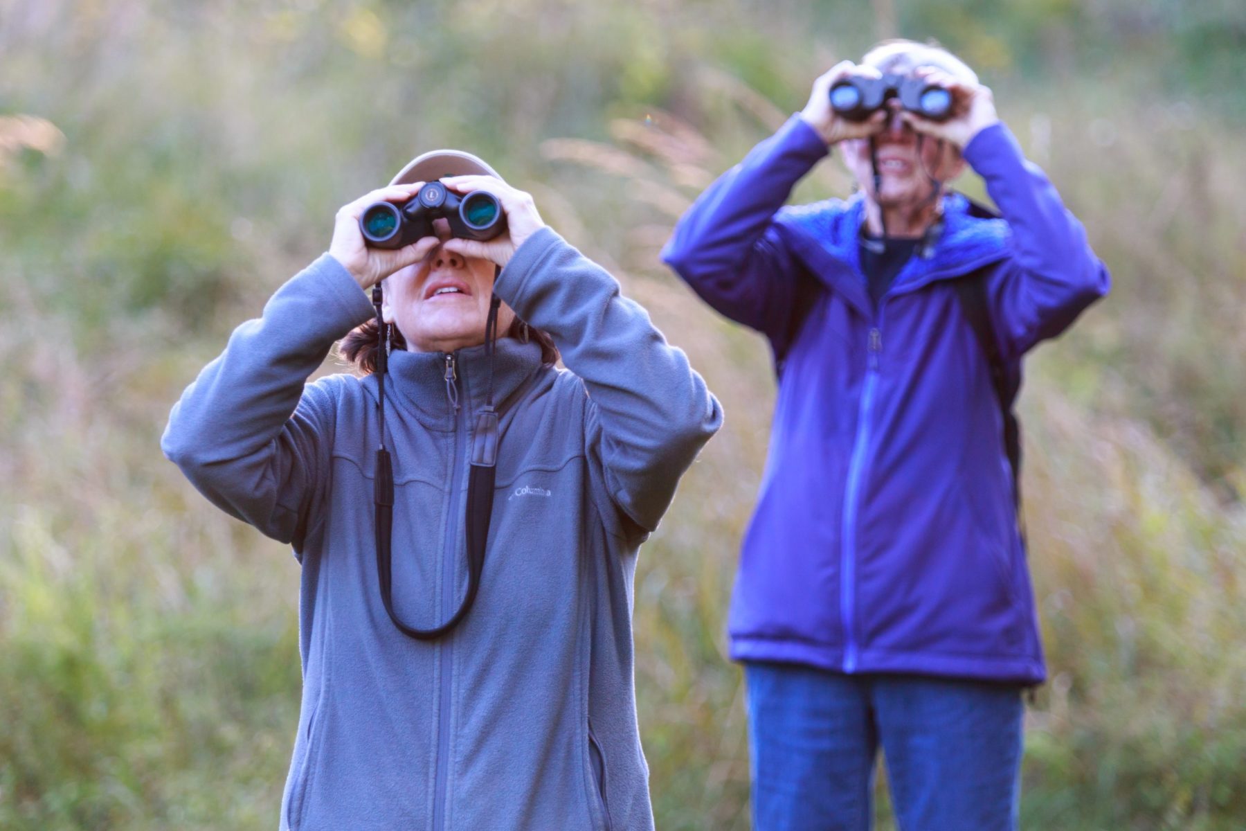 Two people are outside looking towards the sky through binoculars.