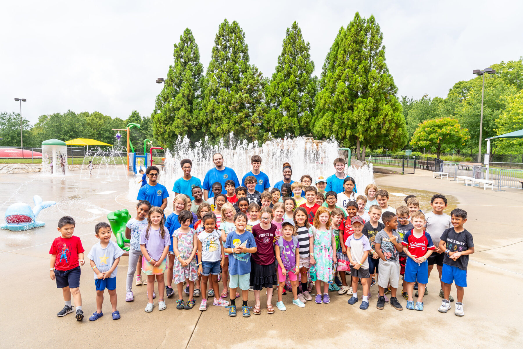 A group of campers are standing in front of water features at a Splash Park.