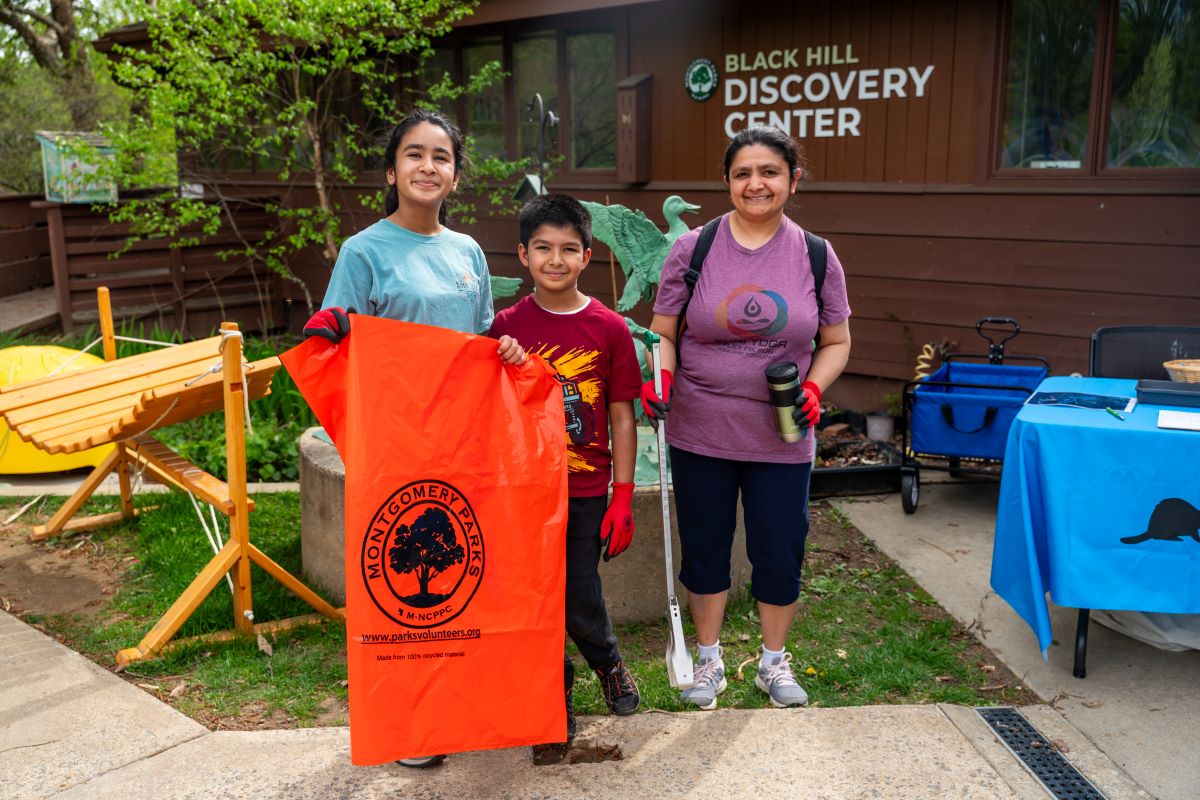 Woman and two children posing with trash cleanup bag.