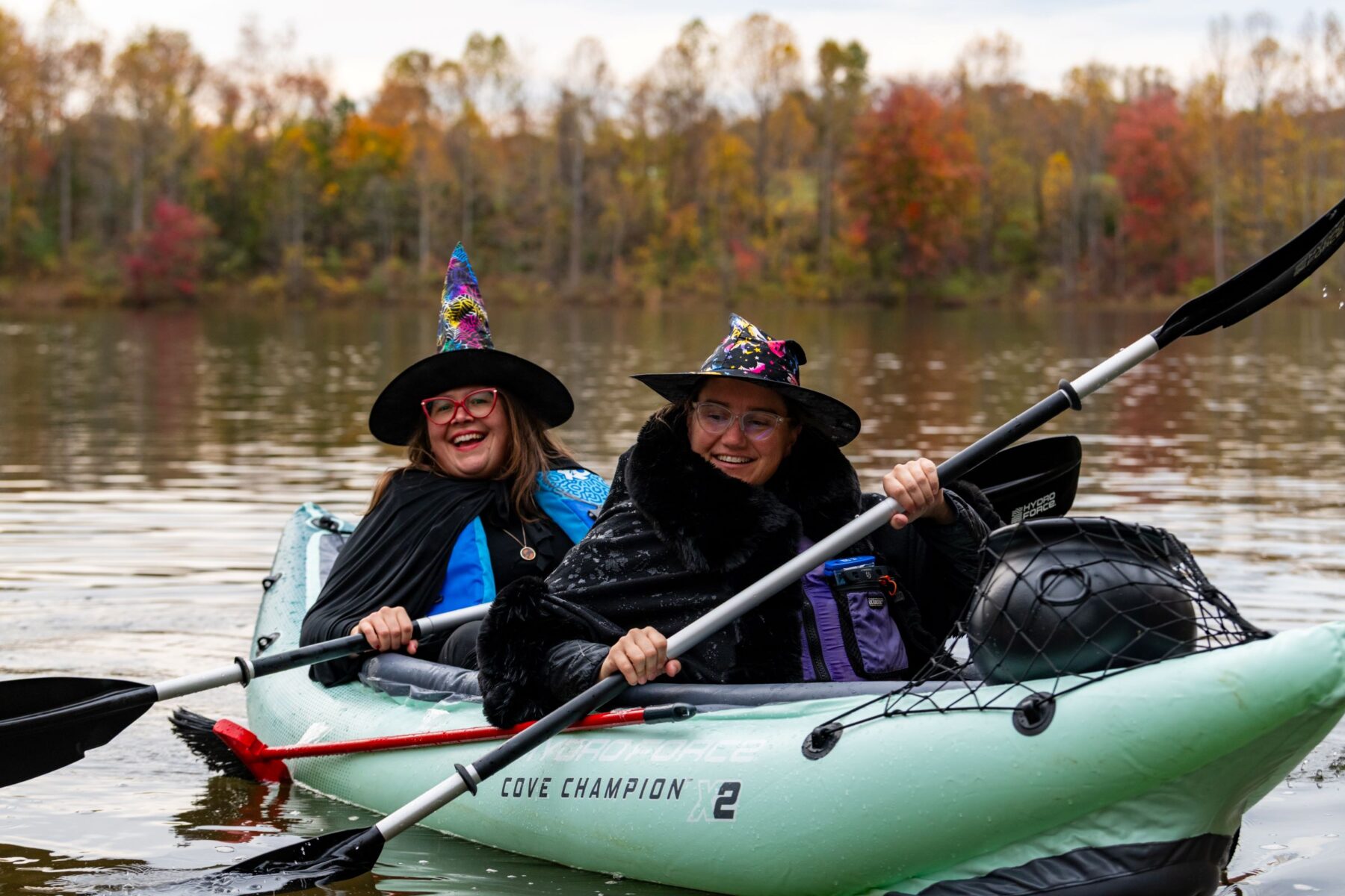Two women paddling a kayaking wearing witches hats