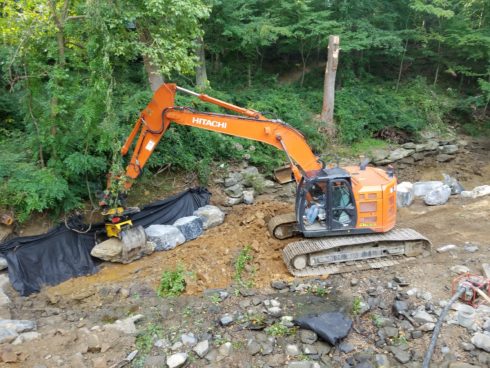 Heavy equipment is used to move stones in a dry stream bed to protect WSSC infrastructure.