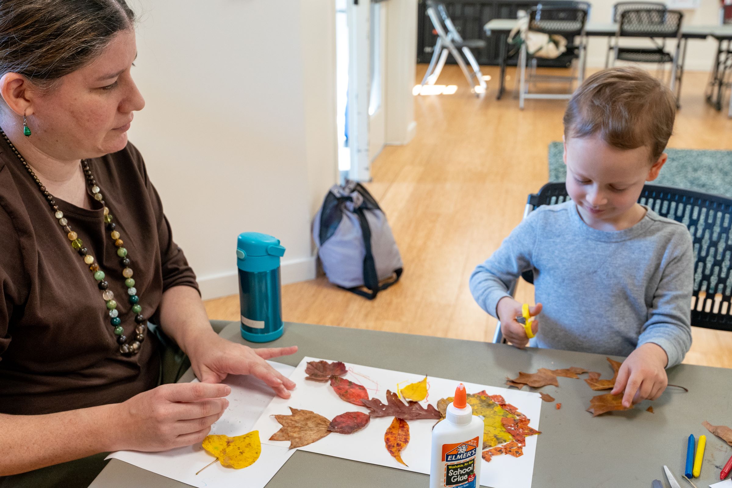 Child cutting with scissors as adult looks on.