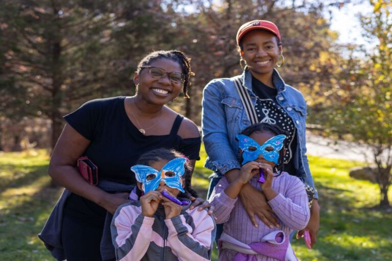 Two women smiling with two children wearing butterfly masks.