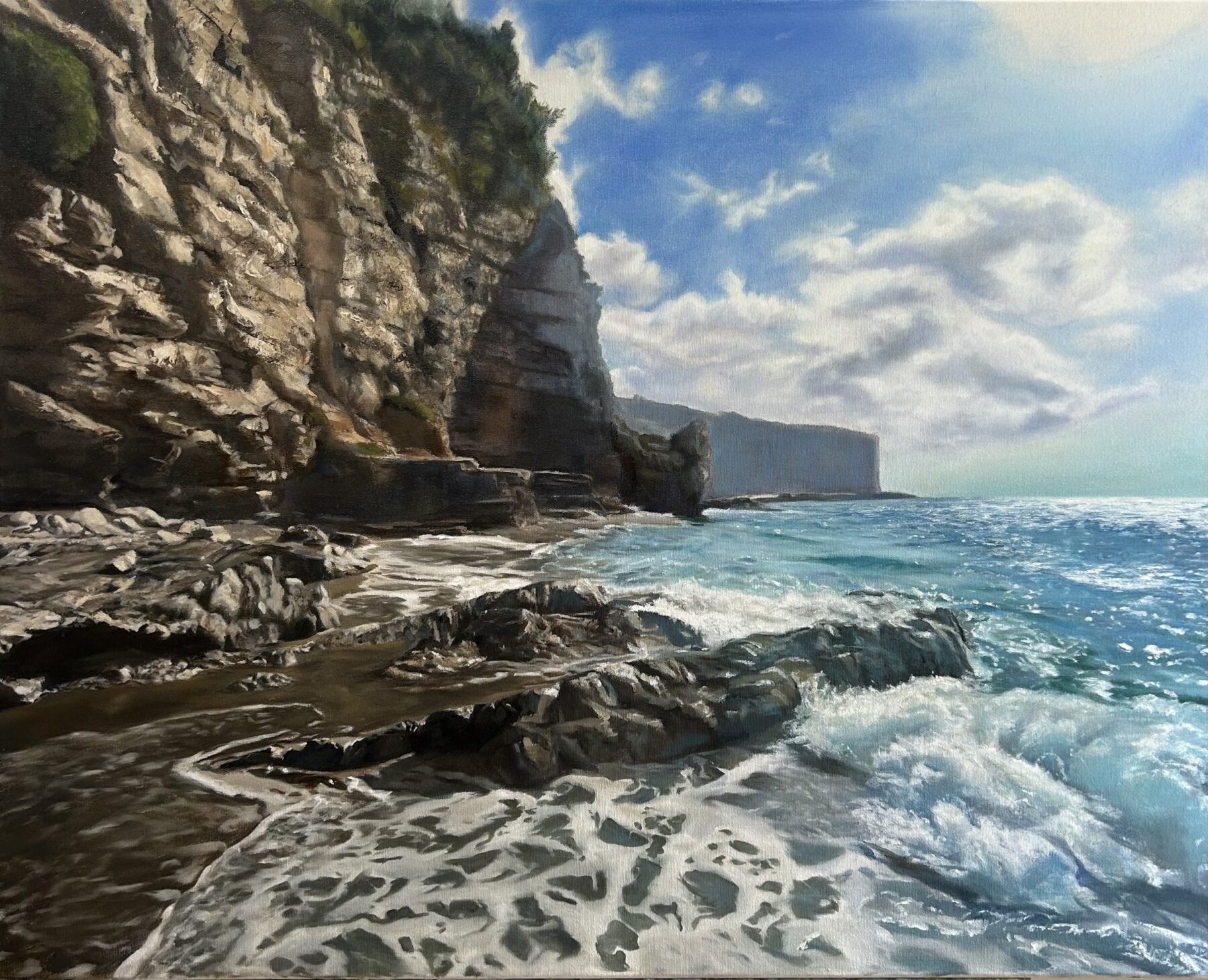 This acrylic painting features rocky cliffs on the left side with patches of green bushes and trees. On the right side is the ocean crashing onto the rocky beach. In the upper right, is a partly cloudy sky against a blue background.