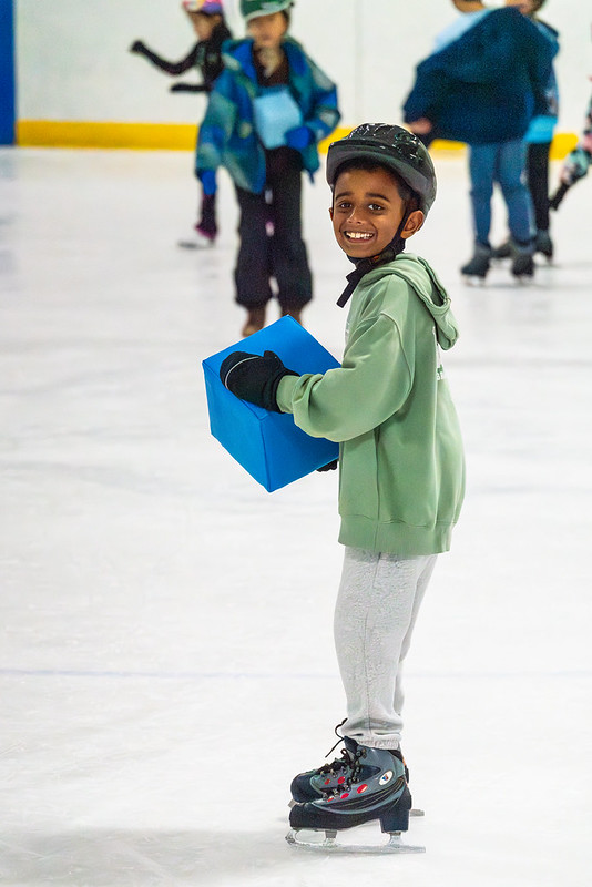Boy smiling and ice skating holding a blue block