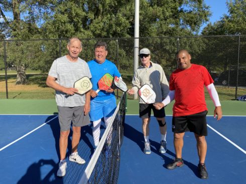 four pickleball player pose for a photo on the court