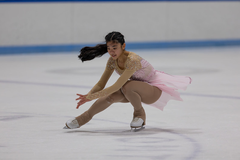 Skater in pink dress performing a sit spin in the ice show