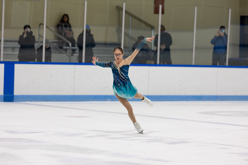 Skater in blue dress performing a leg extension in the ice show