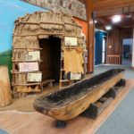 Legacy of the People exhibit with a hut made of straw and branches and a handmade canoe.