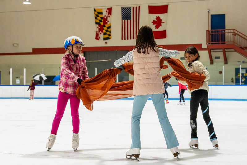 Three Skaters performing with a large orange scarf