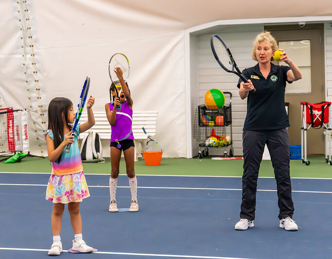 female instructor teaching two children to play tennis