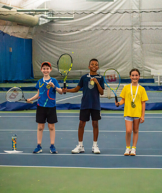 Three children holding tennis racquets and medals