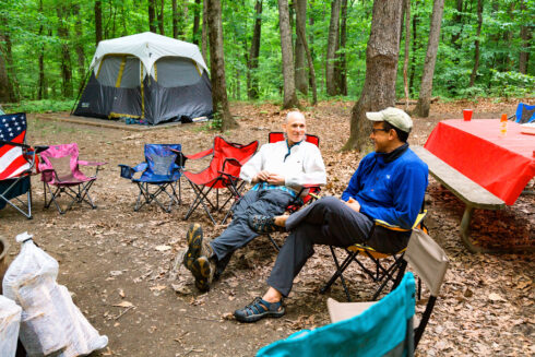 Two adults sit in camping chairs in a wooded area at Little Bennett Camground