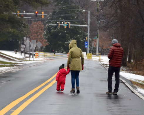Couple and small child in winter coats walk along a wet car-free street with snow on the sides of the road.