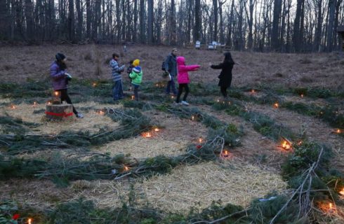 Families dressed in winter coats light candles inside a labyrinth made from pine boughs.