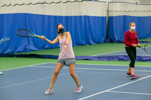 Two adults playing tennis on indoor court.
