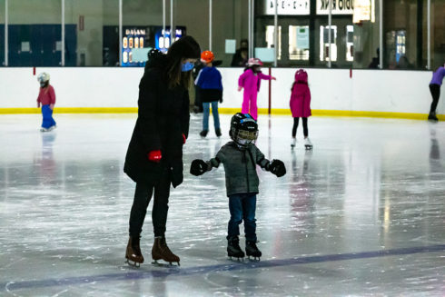 Adult and child skating on indoor ice rink.