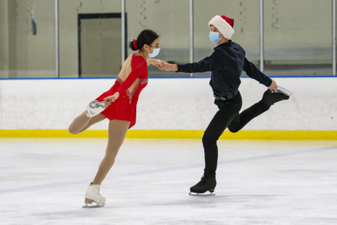 Two skaters performing in ice show on indoor ice rink.