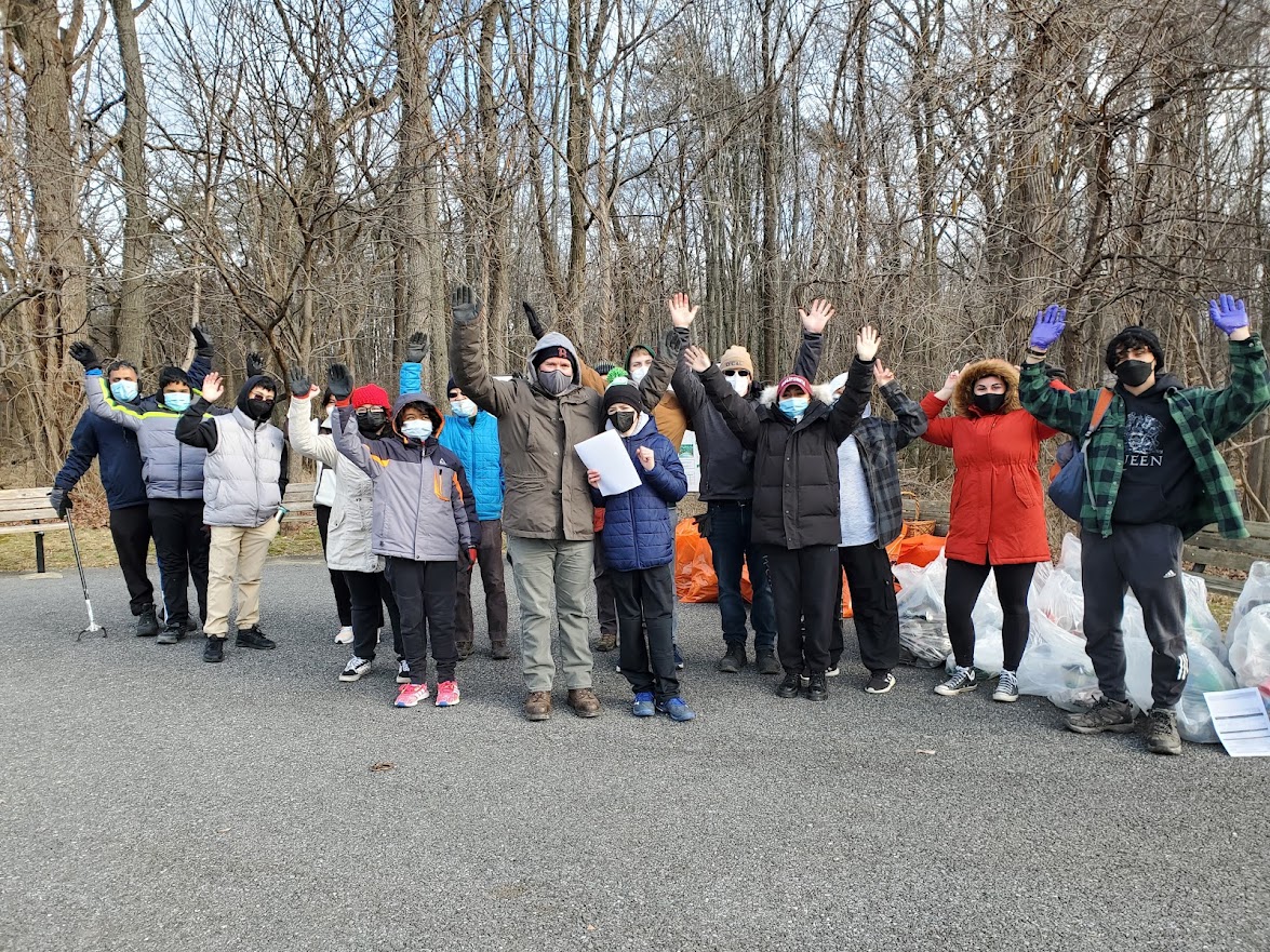 winter, forest background, volunteers with masks and hands up at park after cleanup, trash bags piled behind them