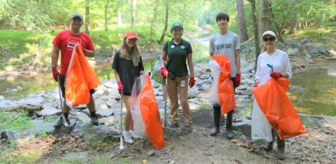 Volunteers cleaning stream with orange bags and a forest in the background