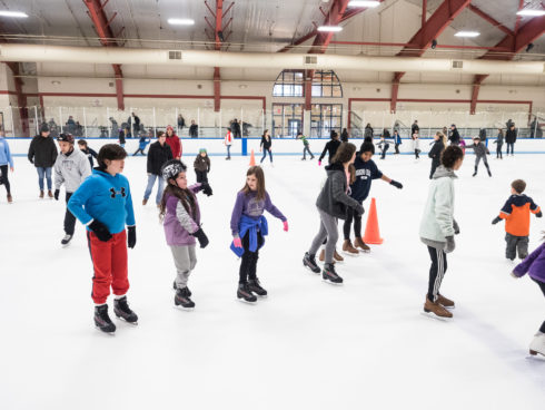 Children ice skating at an indoor rink.