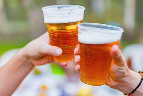 Two hands hold up clear plastic cups filled with beer.