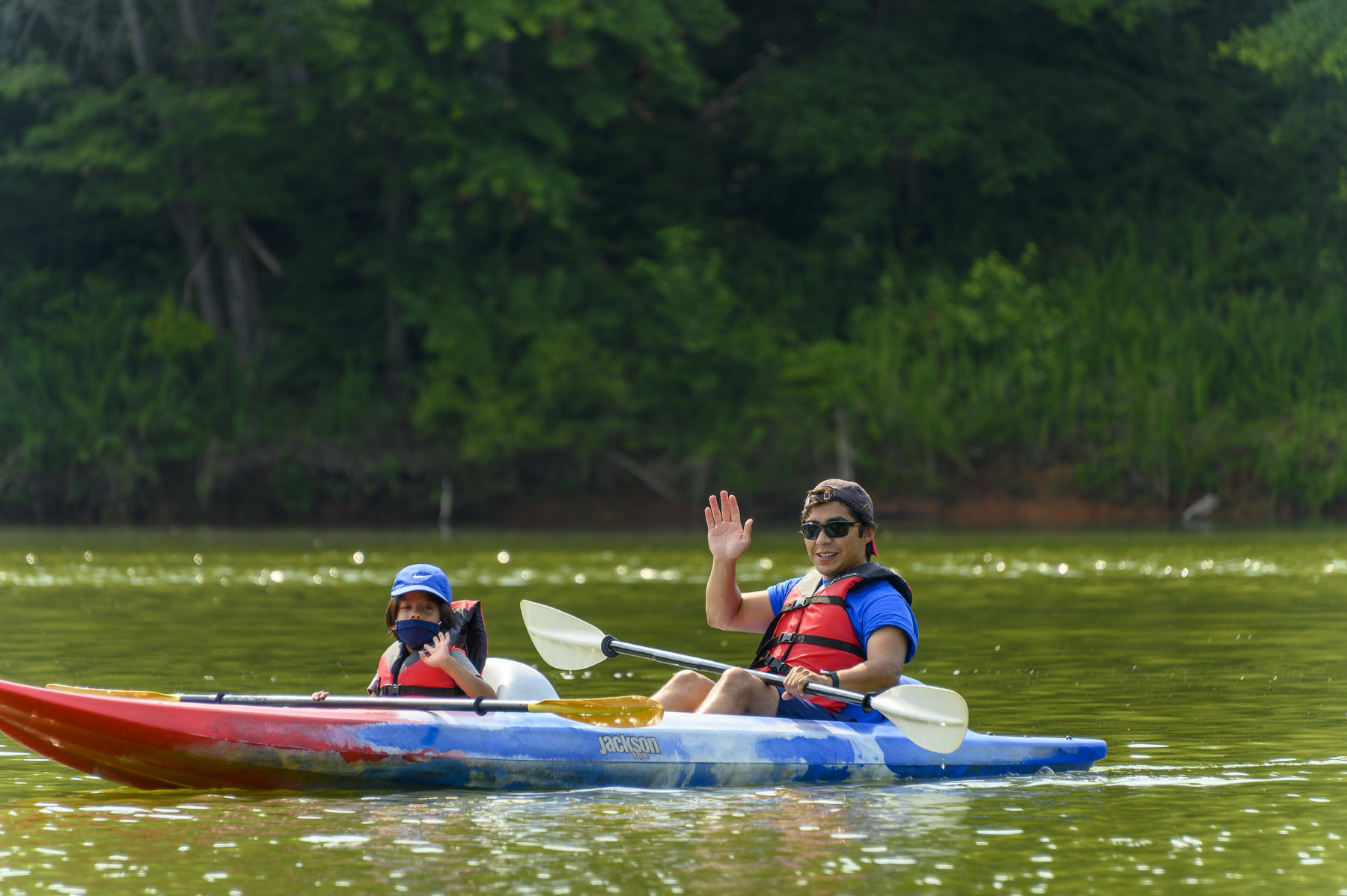 An adult and a child wave from a kayak