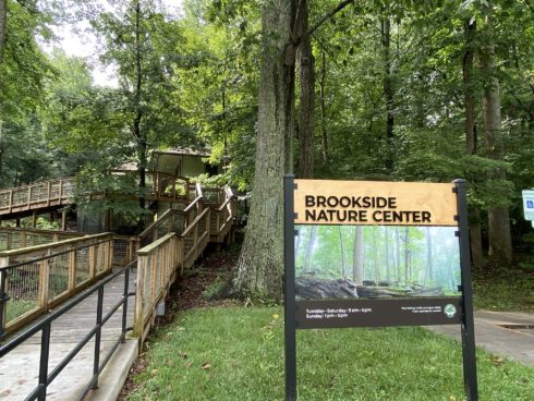 A wooden walkway leading up to Brookside Nature Center. To the right of the walkway is the Brookside Nature Center facility sign.