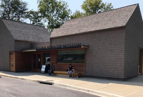 Three people sit on a wooden bench in front of Josiah Henson Museum.