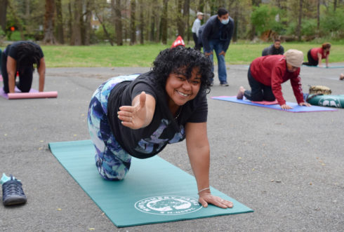 A woman is at an outdoor yoga class. Her arm is outstretched and the other hand is on the mat. 