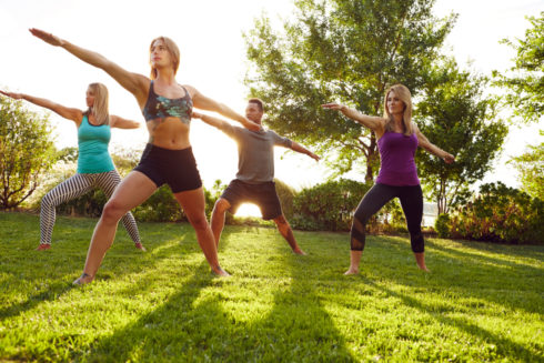Four adults stand in the warrior pose during a yoga session outdoors.