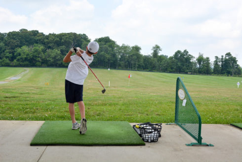 A child wearing shorts, short-sleeved shirt, and hat works on his swing at South Germantown Driving Range.