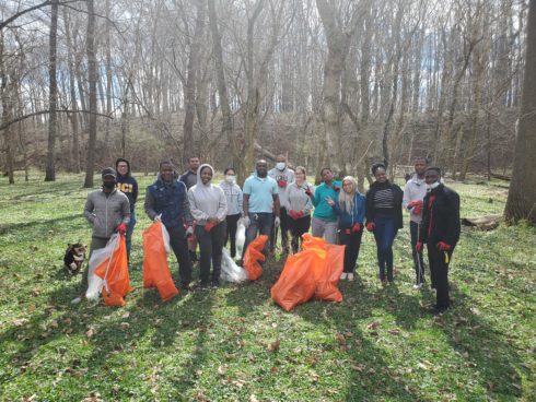 group of volunteers at park cleanup. background of trees and plants. orange trash bags.