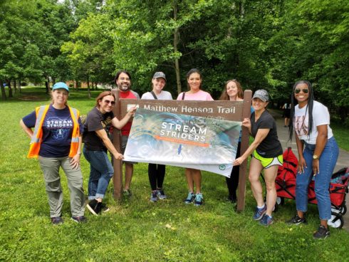 volunteers at matthew henson trail. holding stream striders banner. background of trees and green grass.