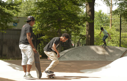 Two skateboarders in the foreground and another skateboarder in the background. They are at a skatepark at Woodside Urban Park in Silver Spring.