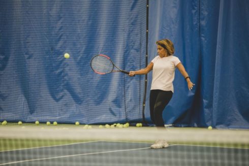 An adult tennis player leans in to hit a tennis ball.