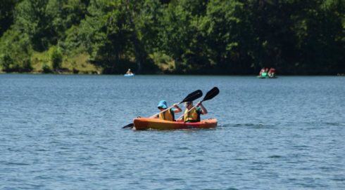 Two people paddling in a double kayak on a lake.