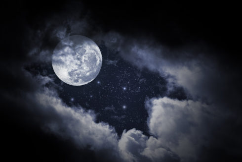 Full moon in the night sky with clouds encompassing it.
