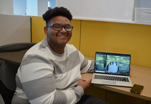Summer Rise student AJ sits at a desk and has a laptop next to him. A slide is up showing a pier at a lake in the park.