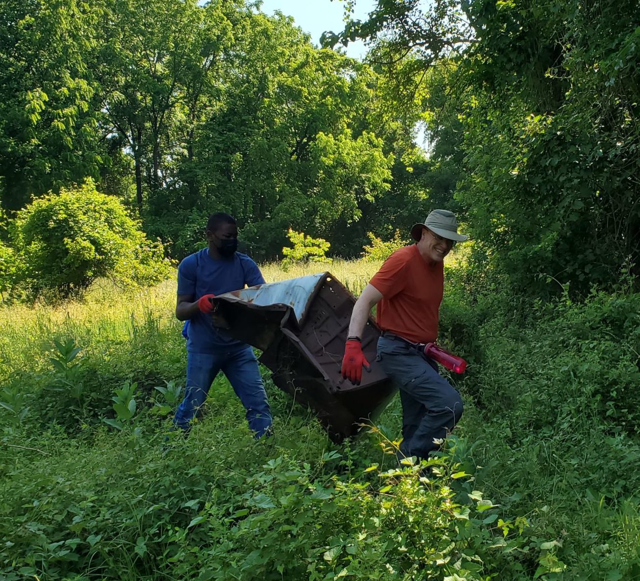 two volunteers in forest carrying a metal box at a volunteer cleanup event