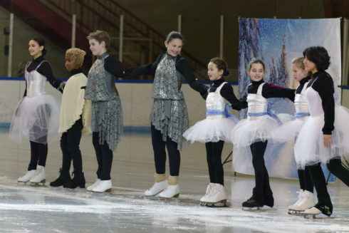 Young ice skaters in silver and white costumes stand in a row during the Winter Ice Show at Wheaton Ice Arena.