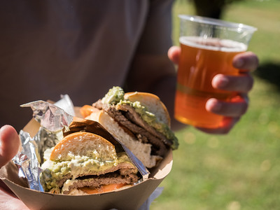 Person holding clear cup of beer and sandwich