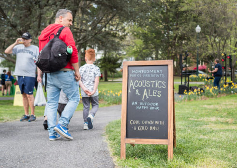 past acoustics and ales welcome chalkboard in focus with people walking by into event