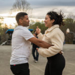 couple facing each other dancing hand in hand with sunset in background
