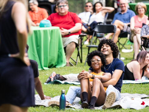 a young couple sitting on a picnic blanket holding each other and smiling as they watch the show