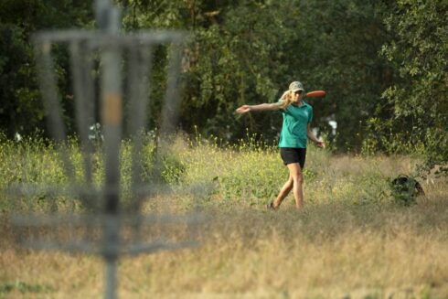 woman throwing a disc into a basket, playing disc golf.
