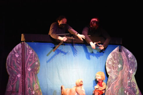 puppeteers controlling marionette peter and cat puppets in woodlands landscape